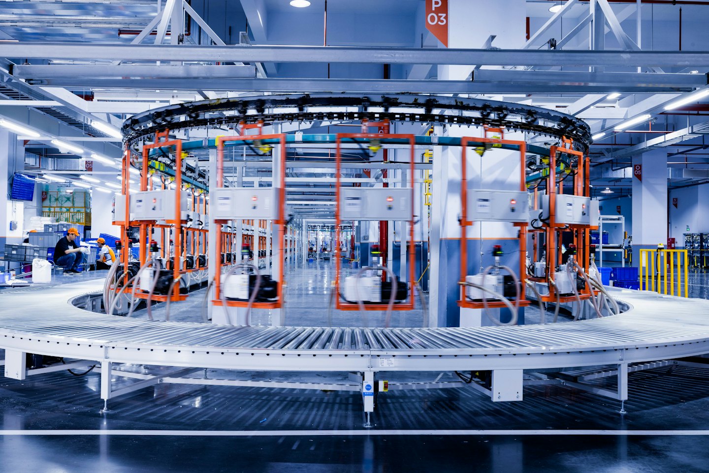Fabrika işçileri, robotik kollara sahip yoğun bir otomatik konveyör sistemini denetliyor.